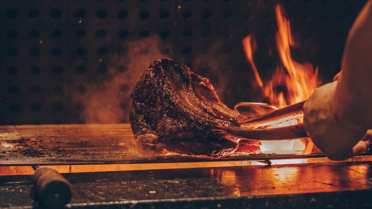 A thick steak searing over open flame on the grill at Fuego