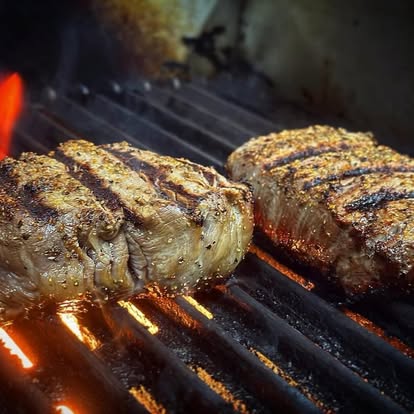 Two steaks searing over open flame on the grill