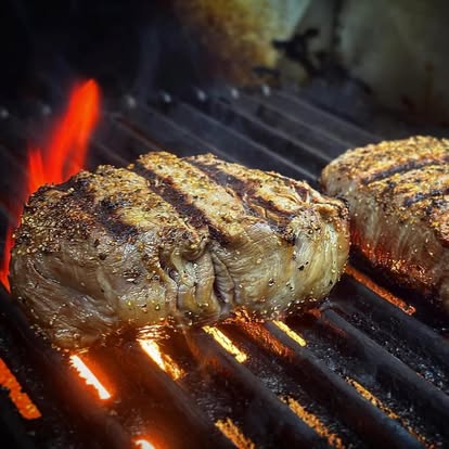 Seasoned steaks cooking over the open flame